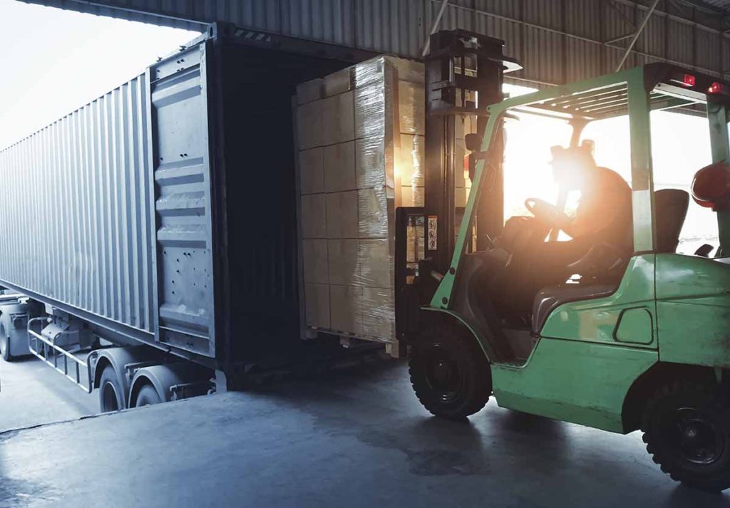 Forklift loading shipment goods pallet into container shipping truck.